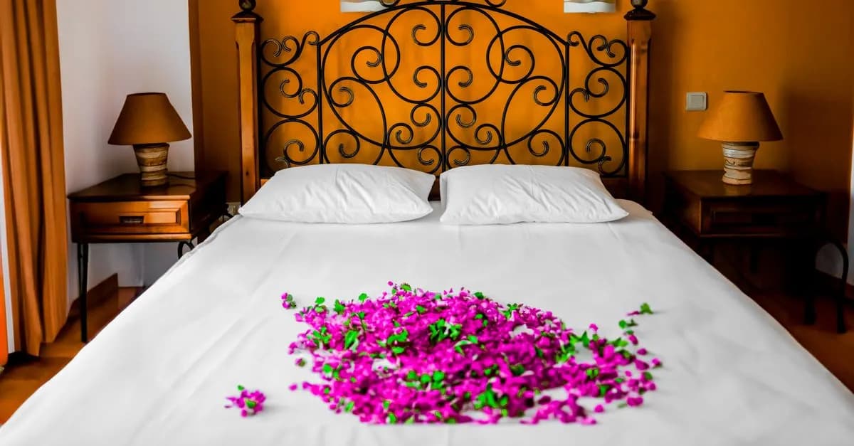 Elegant bedroom with iron headboard and purple petals on white bedding, ideal for romantic getaways.