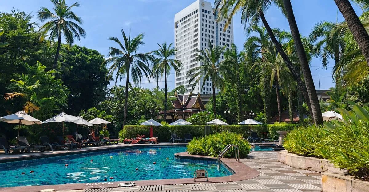 Luxurious tropical poolside setting with a city skyline view on a sunny day.