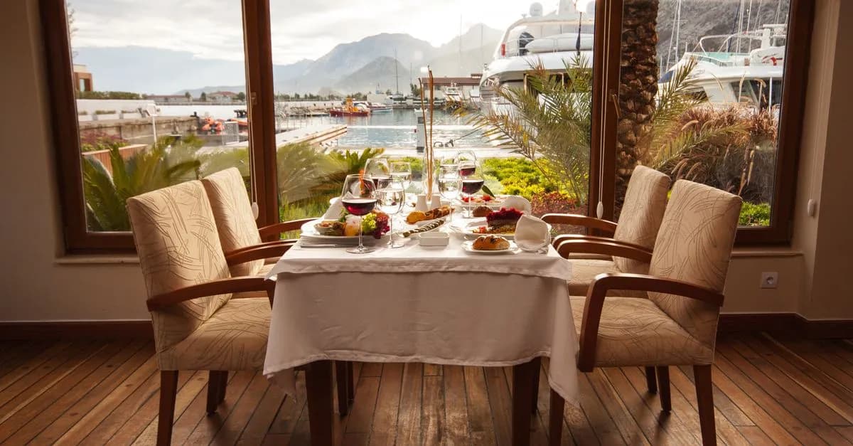 Elegantly set table in a seaside restaurant with a marina view, featuring gourmet dishes and fine dining setup.