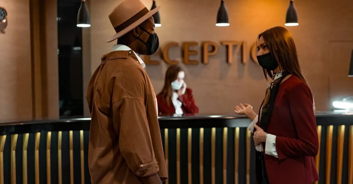 Two people in face masks interacting at a hotel reception desk during the COVID-19 pandemic.
