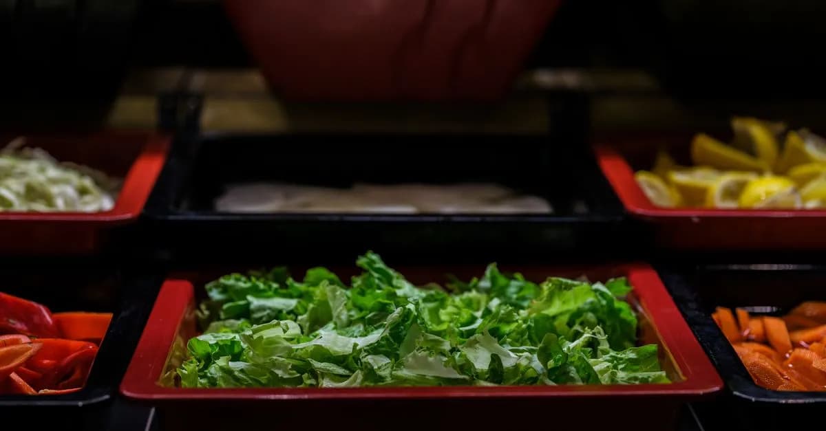Close-up of a vibrant salad bar with fresh vegetables in various trays, offering a healthy dining option.
